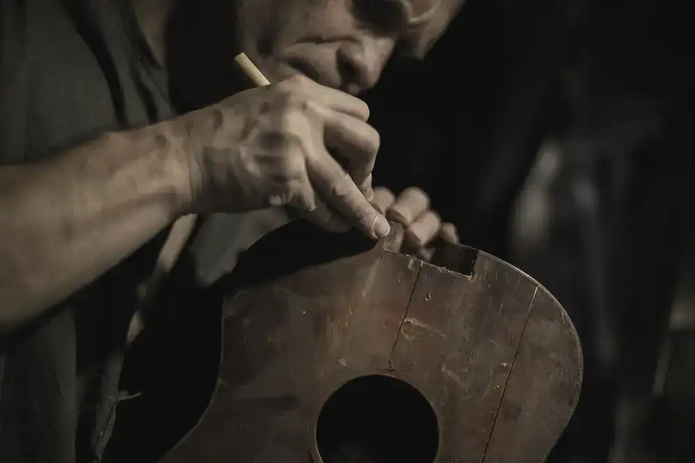 Close up of a luthier adjusting a guitar bridge in a warmly lit workshop